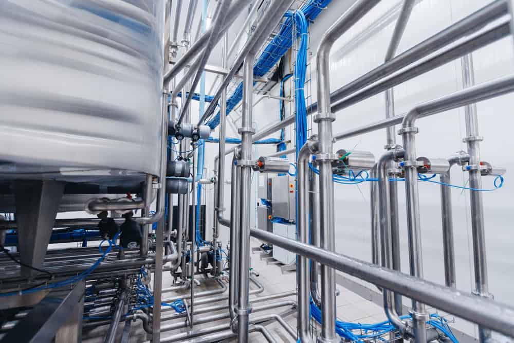 A complex industrial setup with numerous interconnected stainless steel pipes and blue cables. The environment appears clean and structured, likely part of a manufacturing or processing plant, where professional Plumber IL services ensure efficient operations.